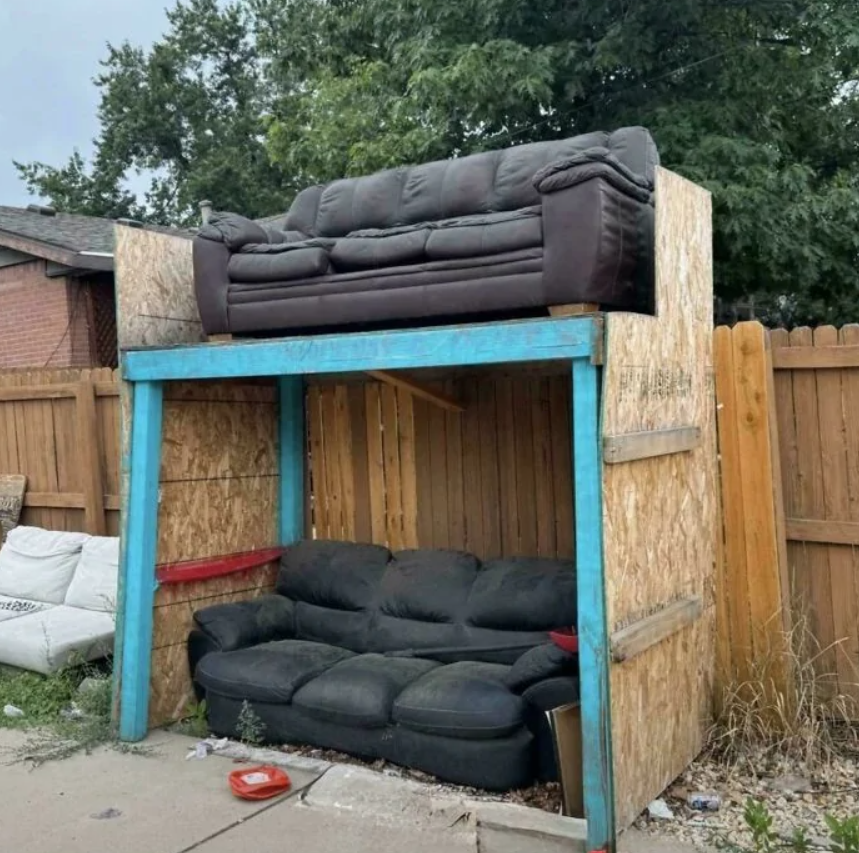 Dve pohovky naskladané na sebe v provizórnom drevenom prístrešku na dvore.