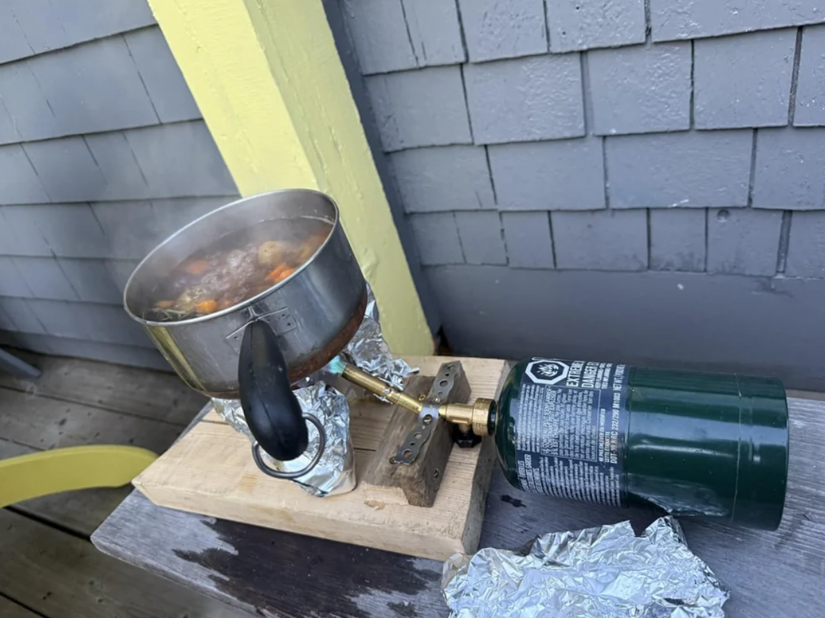 Kanvica s polievkou na provizórnom variči s plynovou bombou na drevenej doske vonku.