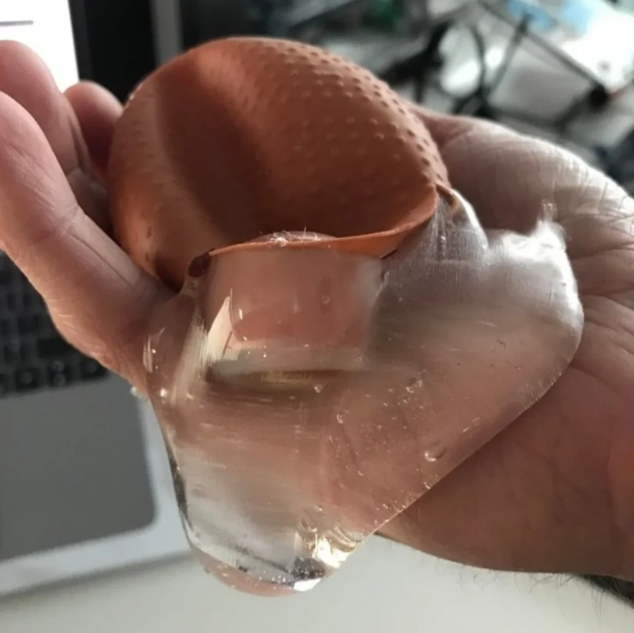 Ruka drží prasknuté vajíčko s čírou tekutinou, v pozadí je vidieť časť klávesnice.