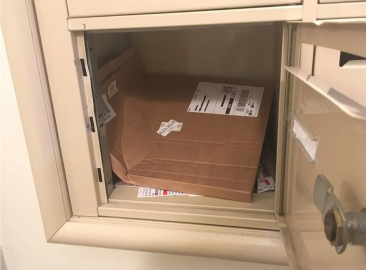 Balík napchatý v príliš malej schránke, s poškodenou krabicou a viditeľnými štítkami na doručenie.