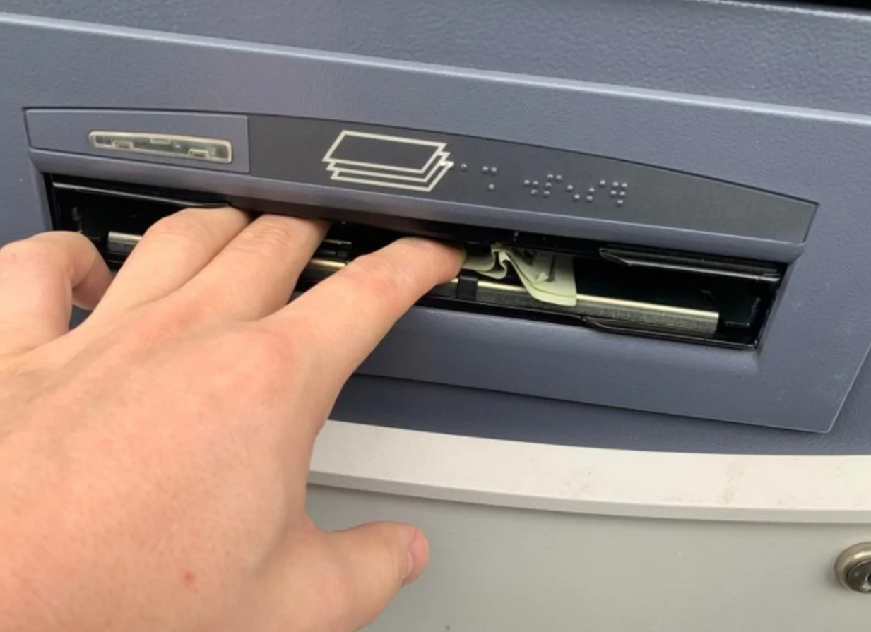 Osoba vyberá hotovosť z bankomatu cez otvor na bankovky.