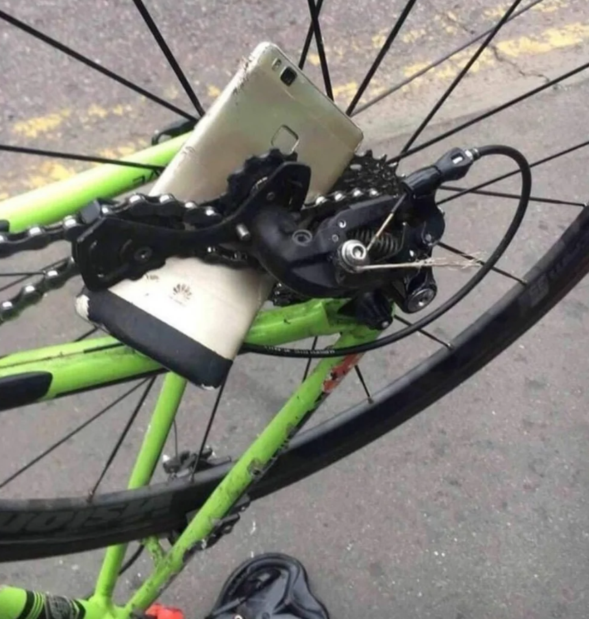 Mobilný telefón uviaznutý v mechanizme bicykla s viditeľným zeleným rámom a zadným prevodom.