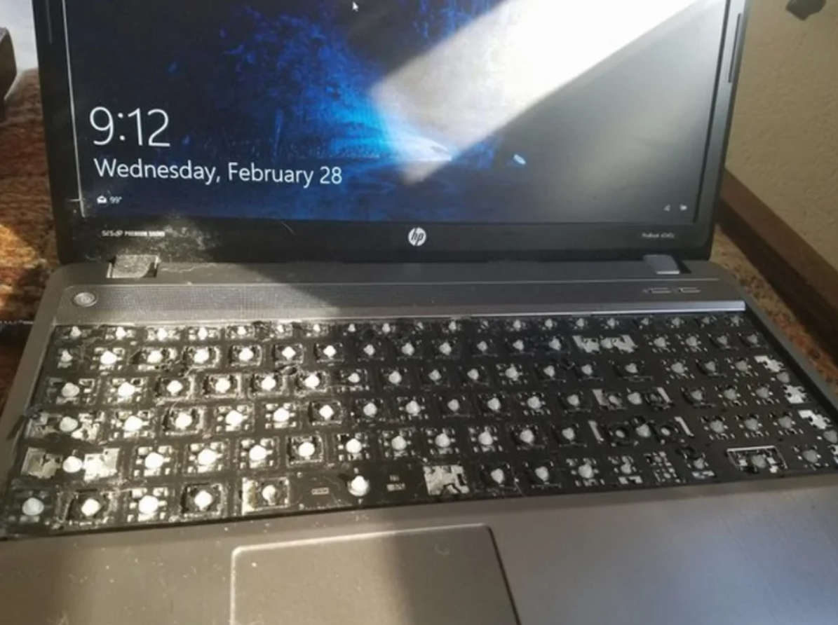 Notebook s poškodenou klávesnicou bez kláves, v pozadí zobrazená uzamknutá obrazovka.