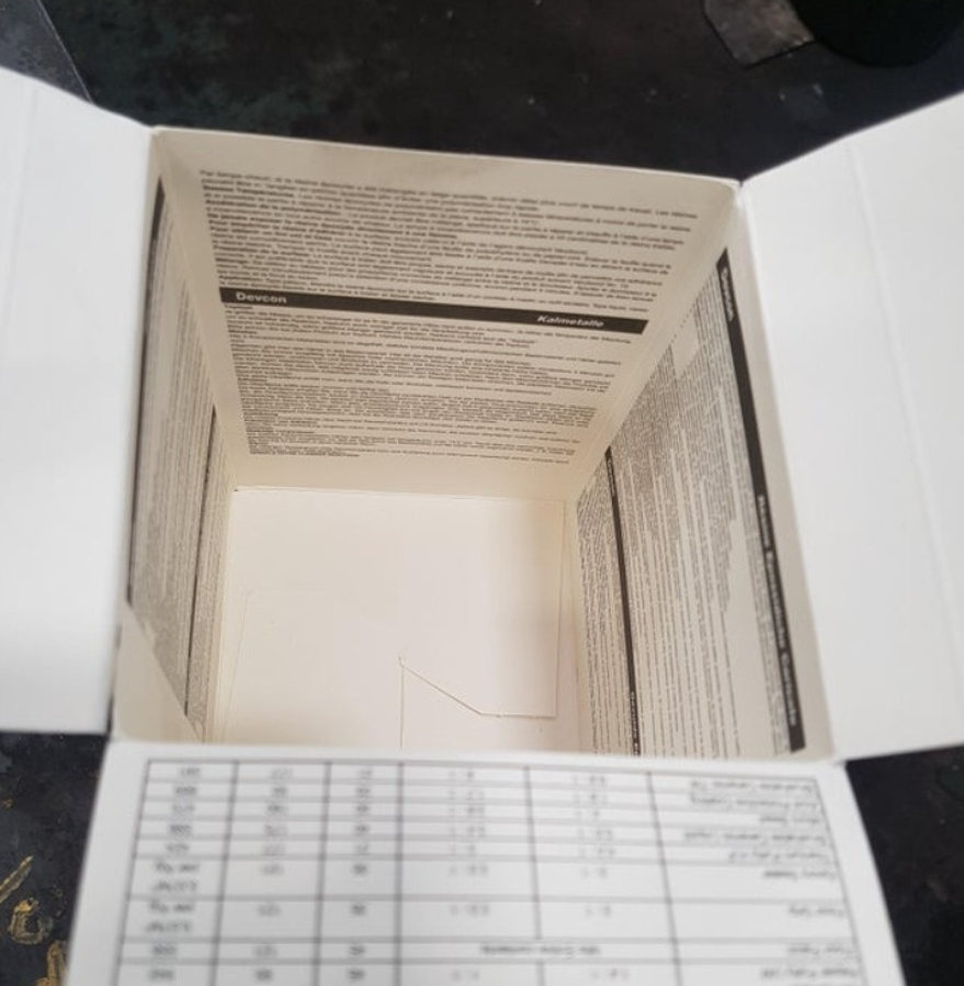 Otvorená kartónová škatuľa s popisom na vnútorných stranách, položená na tmavom povrchu.