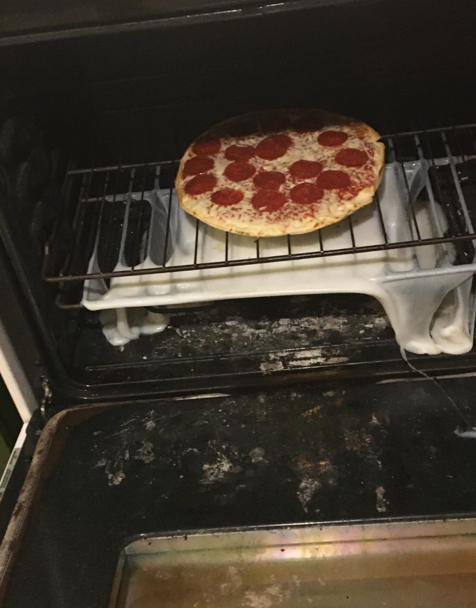 Pizza s pepperoni v rúre, so spáleným pekáčom a vyliatym jedlom pod ňou.