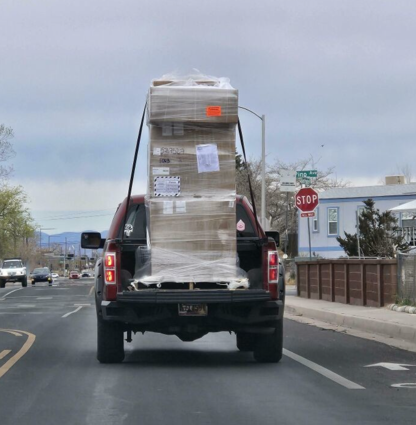 Auto s veľkým nákladom na ulici, obložené krabicami a zabezpečené popruhmi.
