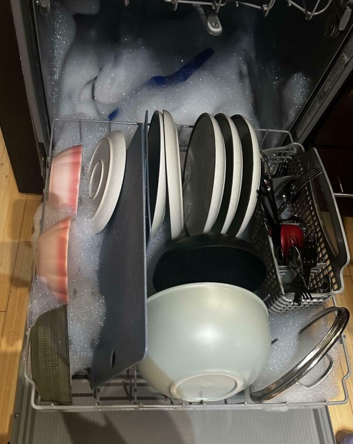 Umývačka riadu plná peny a uloženého riadu po neúspešnom umývaní.