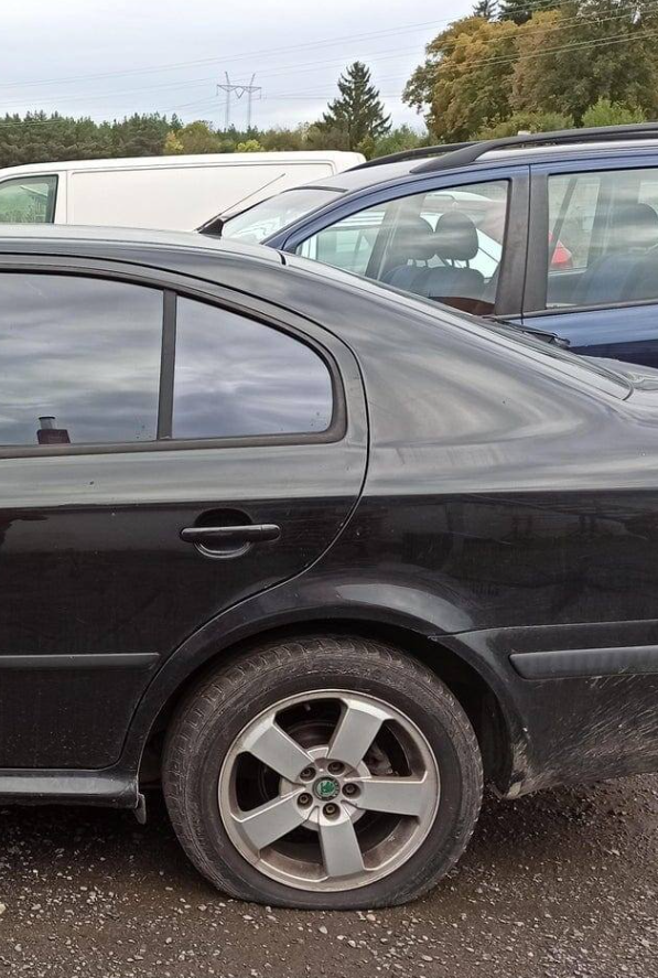 Čierne auto zaparkované vonku s defektom na zadnej pneumatike.