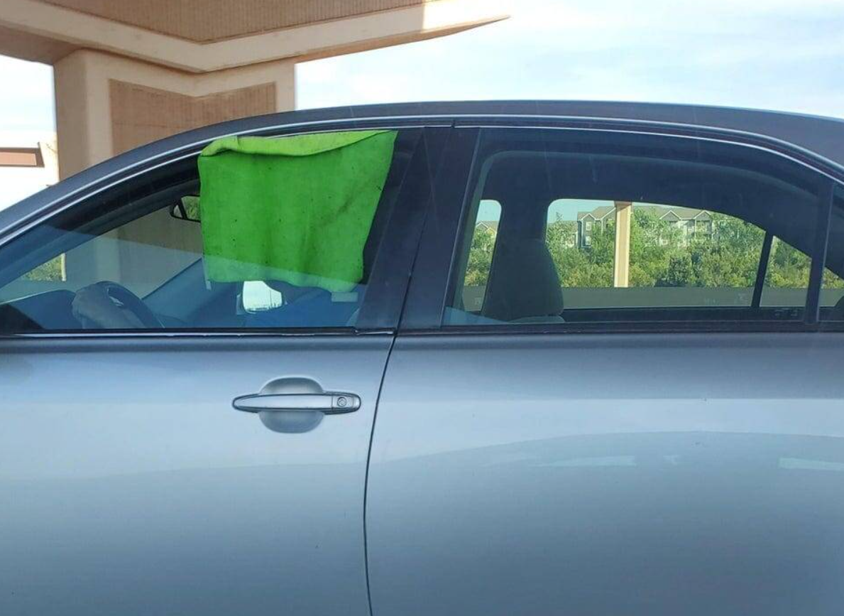 Auto so zelenou handrou na okne, slúžiacou ako provizórna clona proti slnku.