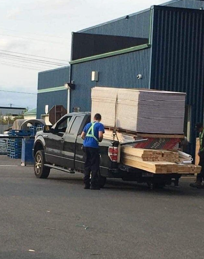Nákladné auto s preťaženým nákladom dreva a sadrokartónu na parkovisku priemyselnej budovy.