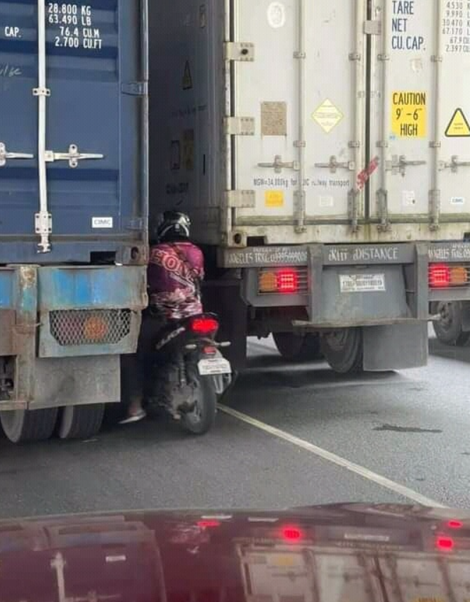 Motorkár medzi dvoma nákladnými autami na ceste ukazuje nebezpečnú jazdu.