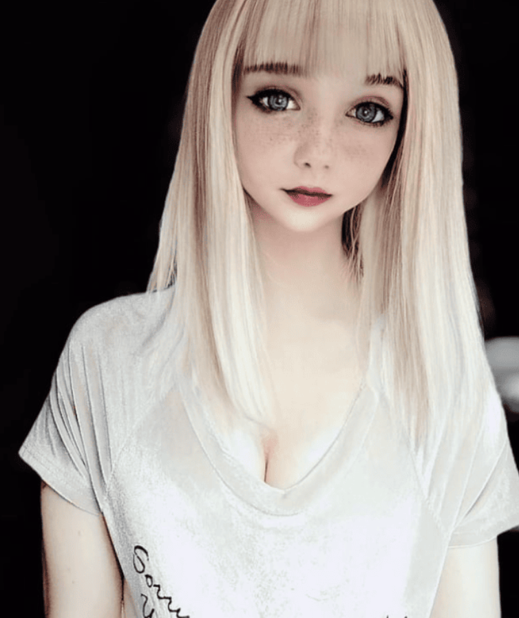 Osoba s dlhými blond vlasmi v svetlom tričku pozerajúca priamo na objektív fotoaparátu.