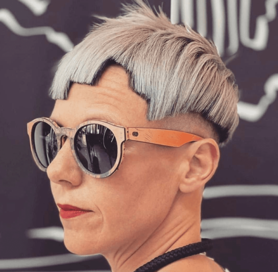 Osoba s extravagantným účesom a slnečnými okuliarmi na retro pozadí.