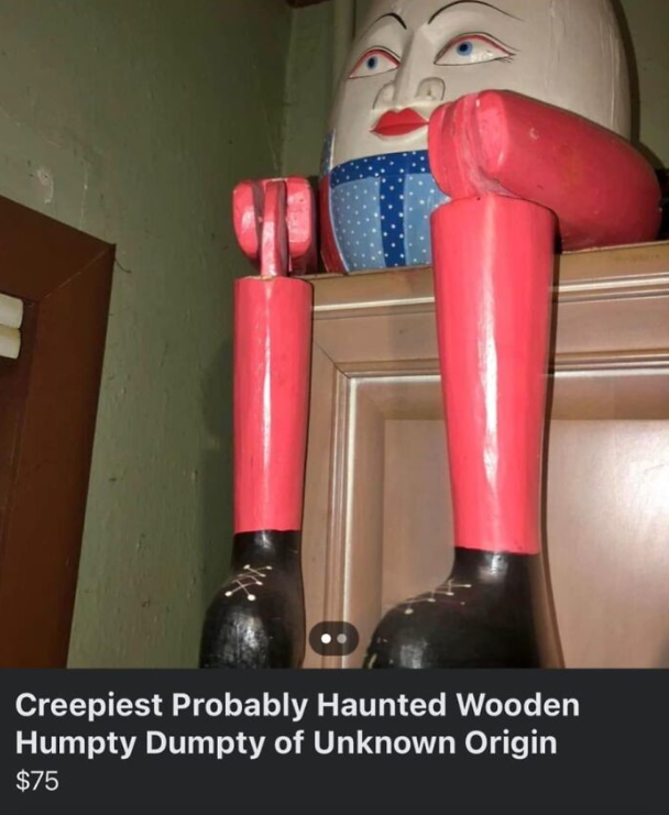 Drevená soška Humpty Dumpty v pestrých farbách na skrini, pôsobiaca záhadne a strašidelne.