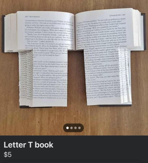 Otvorená kniha vyrezaná do tvaru písmena T položená na drevenom stole.