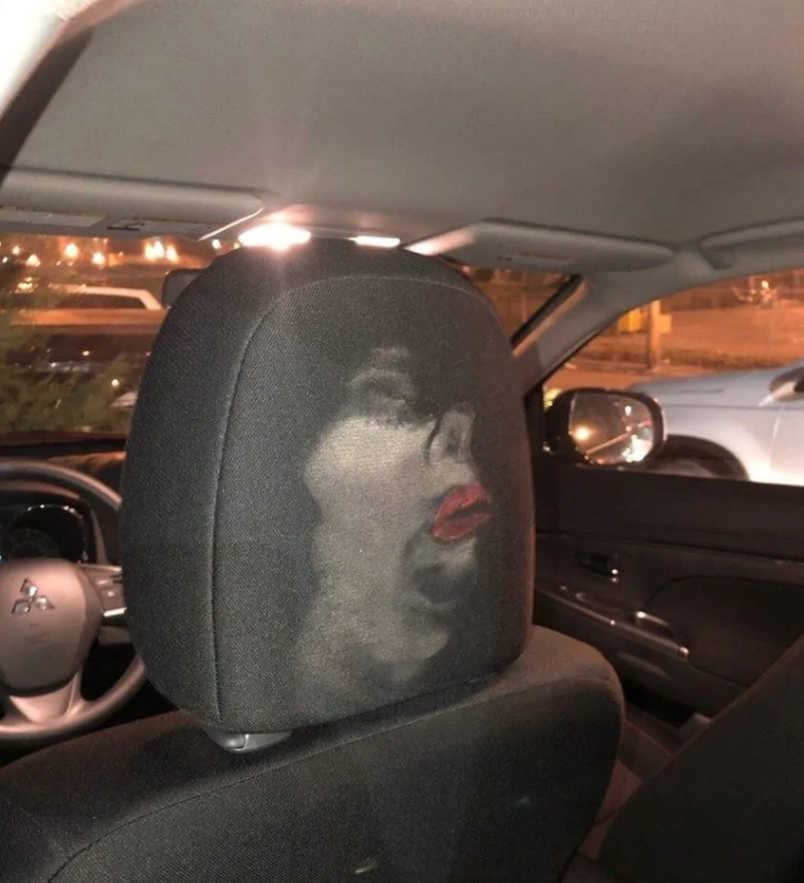 Kresba tváre ženy s výrazom údivu na opierke hlavy v aute počas večera.