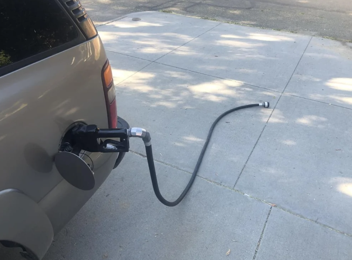 Auto s benzínovou hadicou pripojenou k nádrži na asfalte, chyba pri tankovaní.