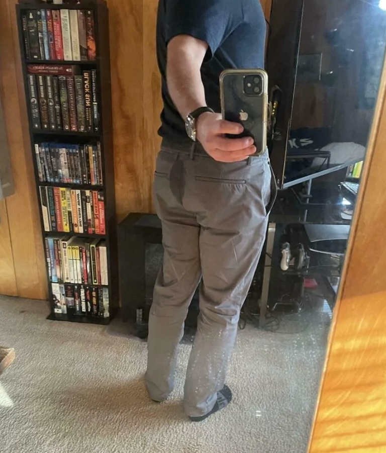 Osoba vo svetlých nohaviciach stojí pred zrkadlom v izbe s knihami a zrkadlí sa cez smartfón.