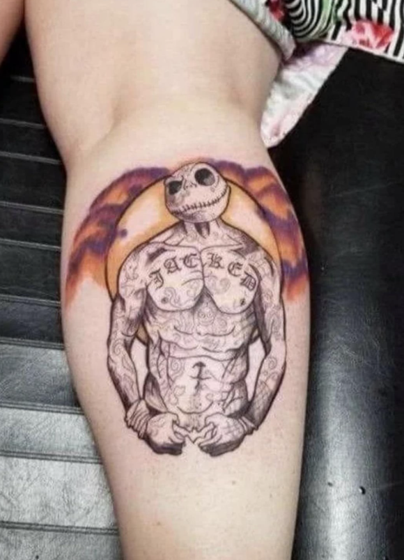 Tetovanie s postavou kostlivca s nápisom JACKED na hrudi, obklopené farebným pozadím na stehne.