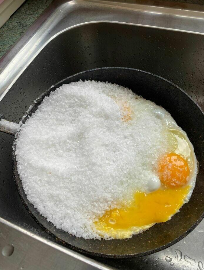 Panvica s rozbitými vajíčkami, pokrytými veľkým množstvom soli, položená v kuchynskom dreze.