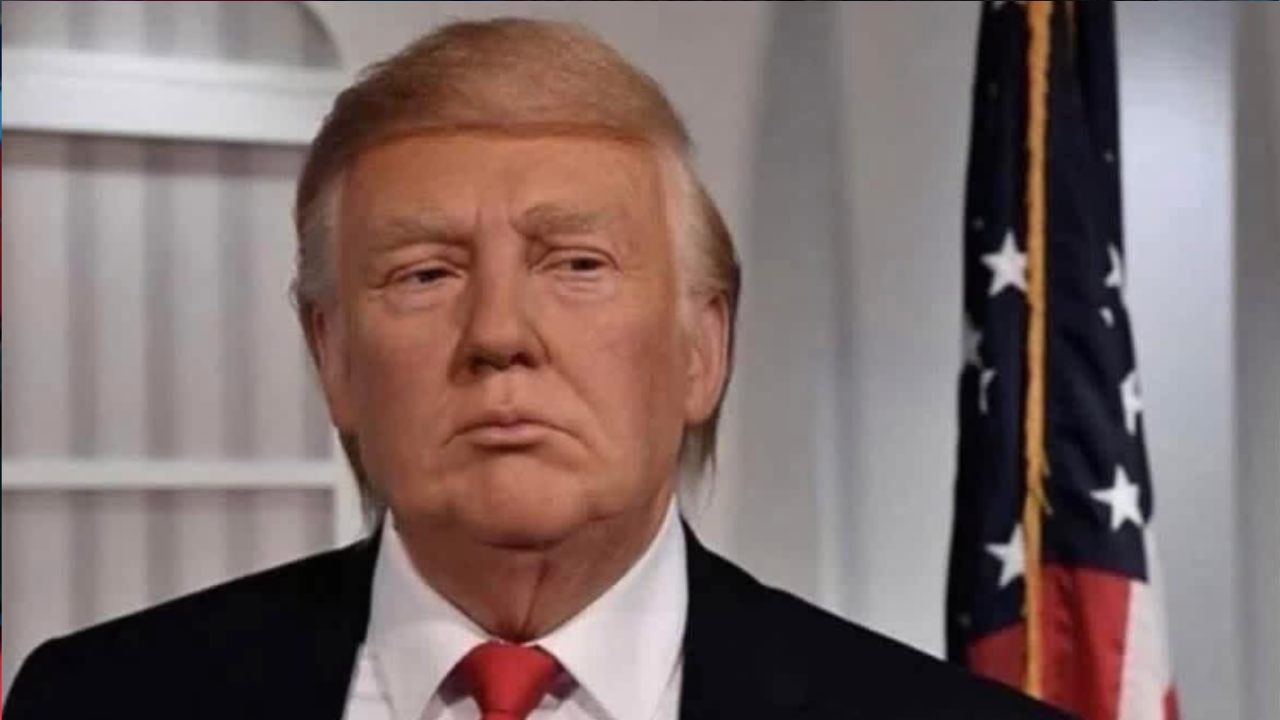 Ostrihovaný muž v obleku pred vlajkou v kancelárskom prostredí.