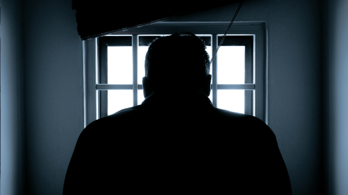 Silueta človeka stojaceho pred oknom s mrežami, pohľad z interiéru.