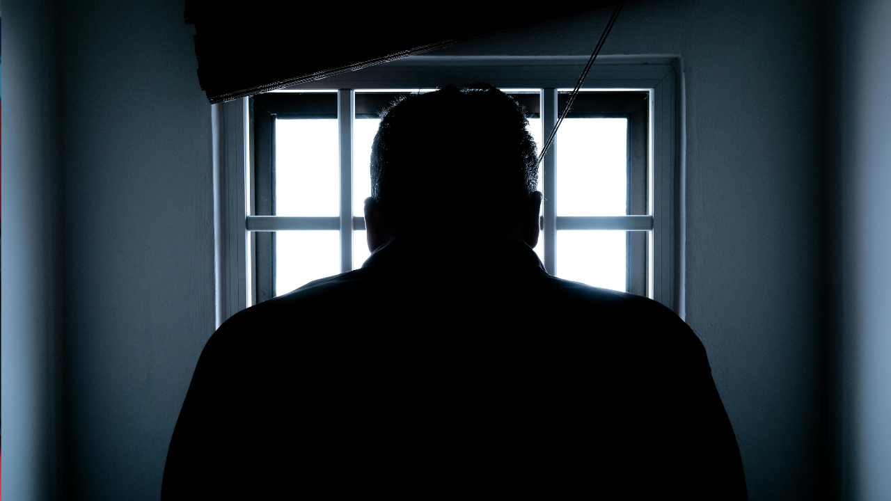 Silueta človeka stojaceho pred oknom s mrežami, pohľad z interiéru.