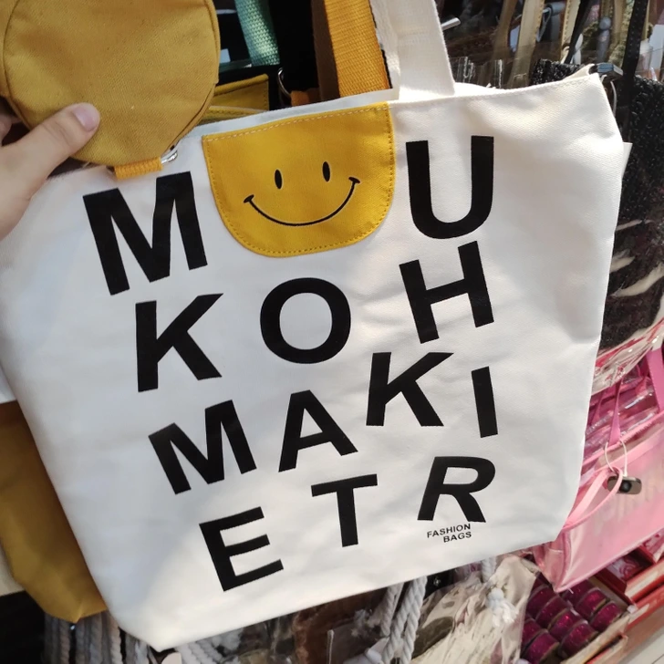 Biela taška s čiernymi písmenami, ozdobená veselým žltým smajlíkom.