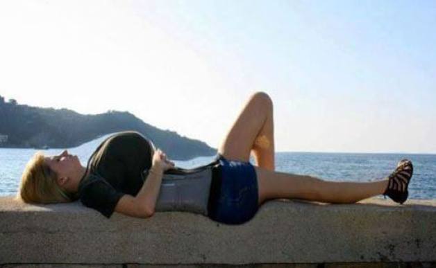 Žena ležiaca pri mori na kamennej stene, relaxuje pod jasnou oblohou.