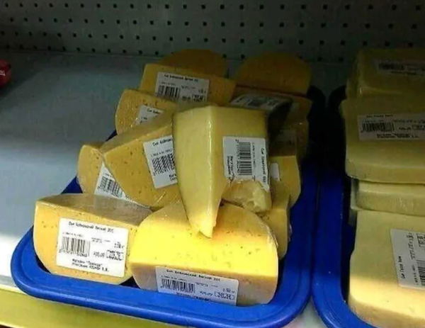 Kúsky syra s etiketami na plastovom tácke v obchode, vystavené na polici.