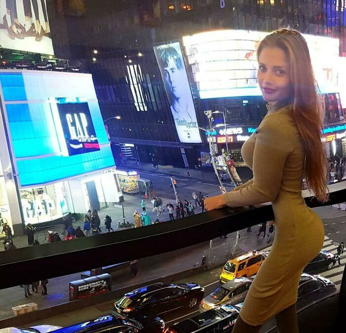 Osoba na balkóne s výhľadom na rušnú mestskú ulicu s neónovými reklamami v noci.