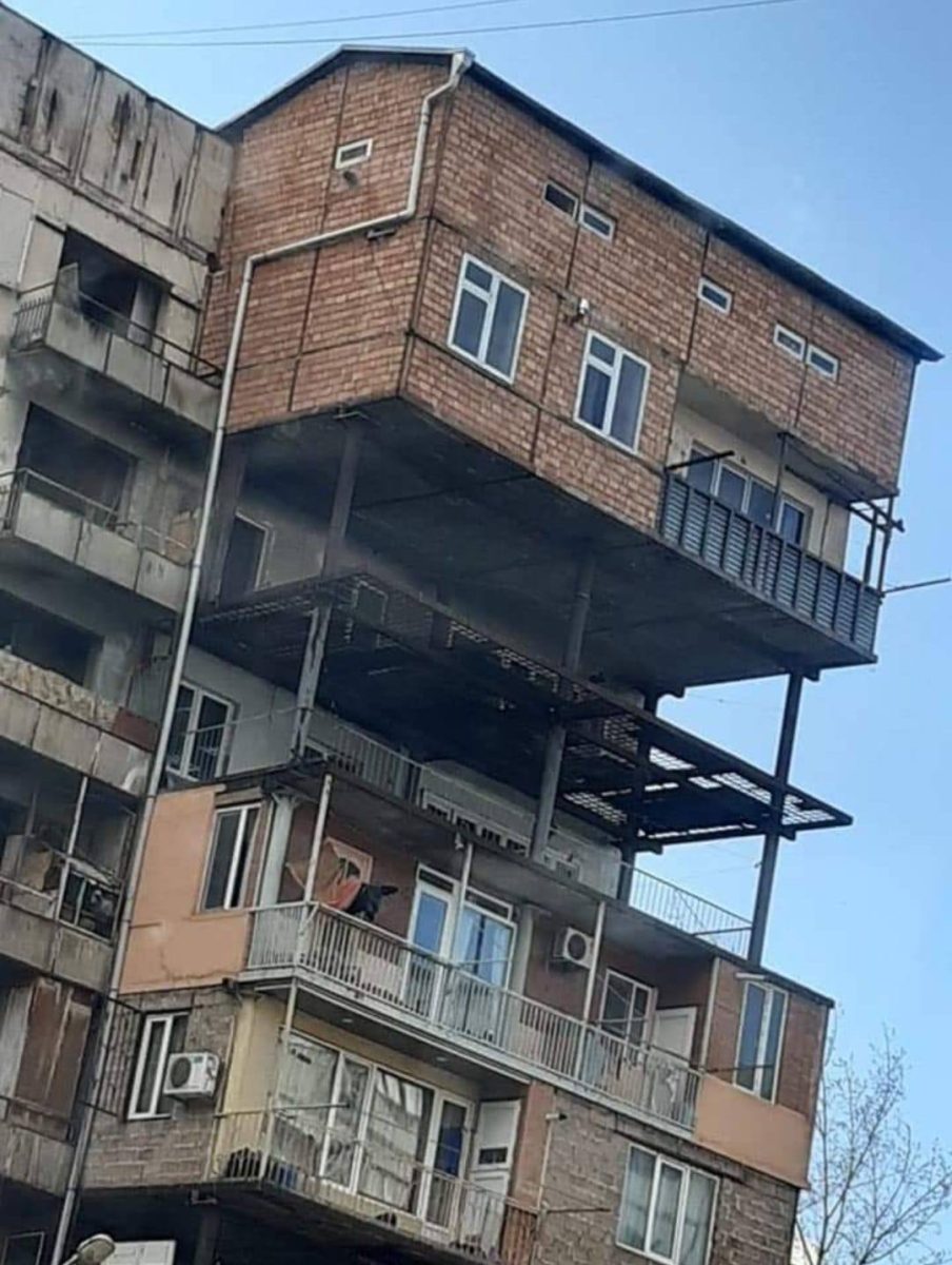 Neobvyklé stavebné rozšírenie paneláku s drevenou prístavbou na vrchole, vyčnievajúce mimo pôvodnej konštrukcie.