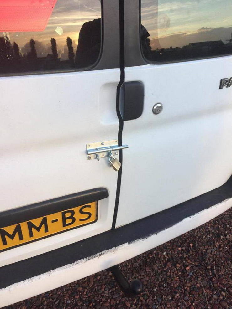 Biele zadné dvere dodávky uzamknuté visacím zámkom pre dodatočnú bezpečnosť, podvečerné osvetlenie v pozadí.