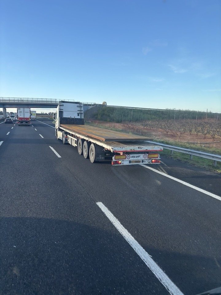 Kamión s návesom bez nákladu jazdí po diaľnici pri modrej oblohe, vedľa neho sa rozprestiera krajina.