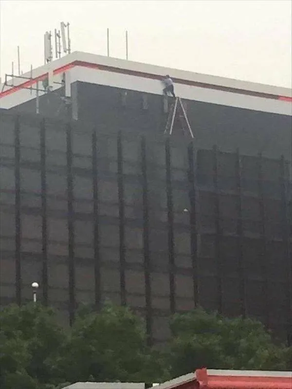 Osoba na rebríku opravuje vysokú budovu bez adekvátneho zabezpečenia.