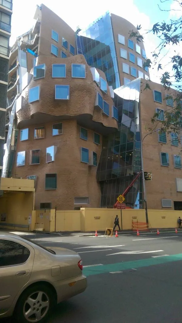 Moderná architektúra s nepravidelnými tvarmi a sklenenými fasádami na rušnej ulici.