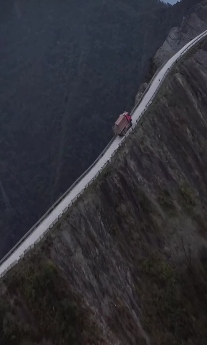 Nákladné auto na horskej ceste, obklopené strmými svahmi a hustými lesmi. Vertikálna perspektíva.