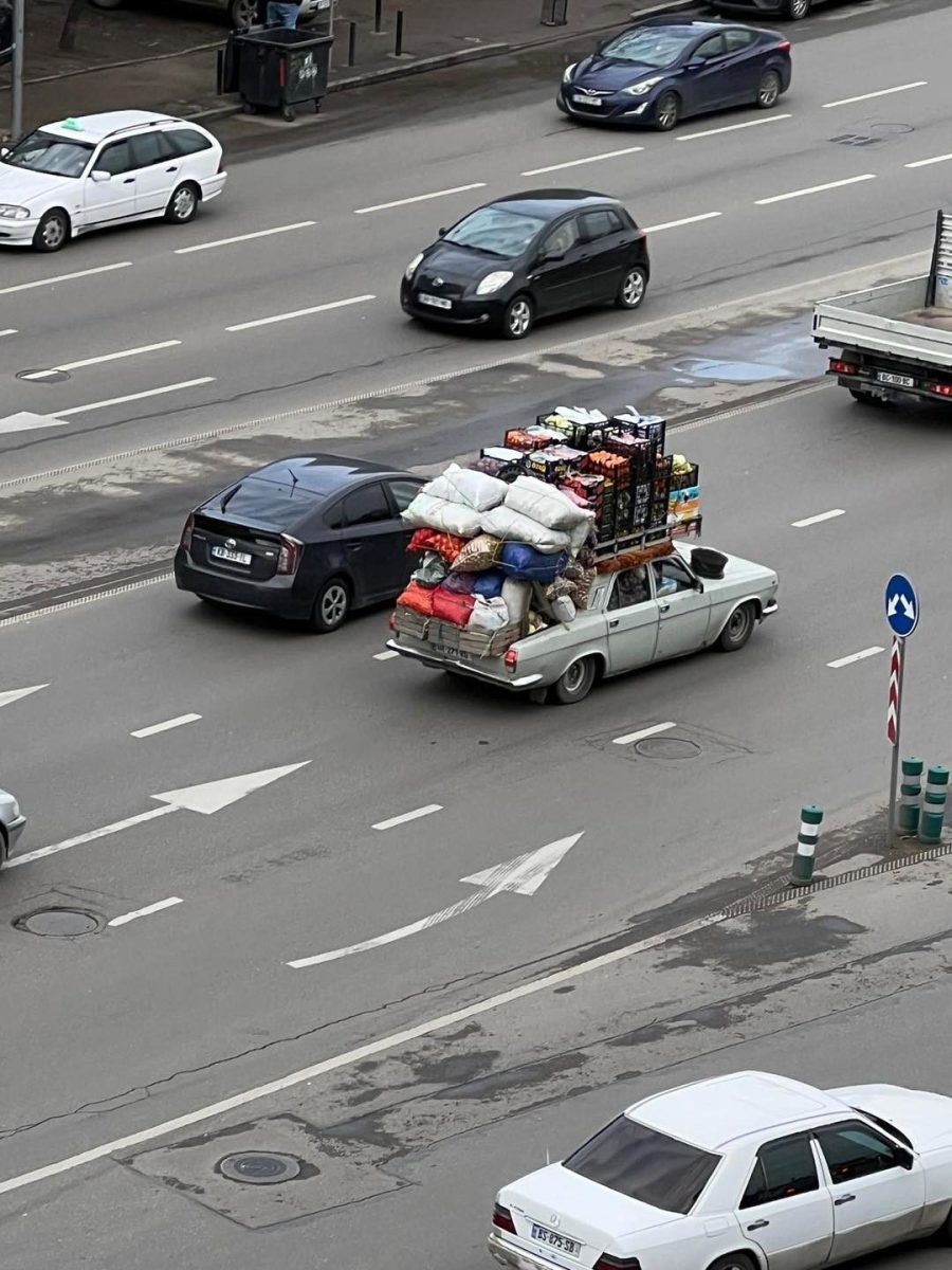Auto s preťaženou strechou vezie veľa batožiny a nákladu po rušnej mestskej ceste.