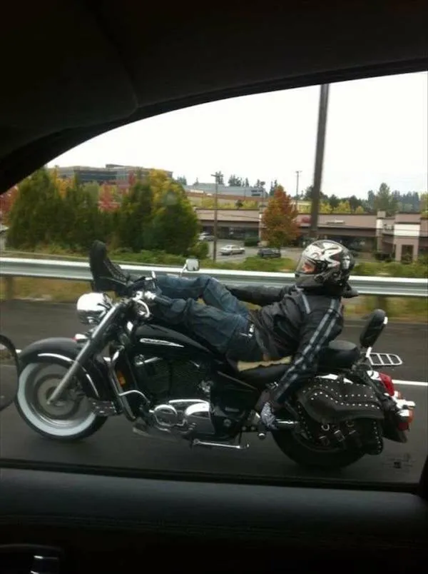 Motorkár v prilbe so zloženými nohami na motorke pokojne jazdí po diaľnici.