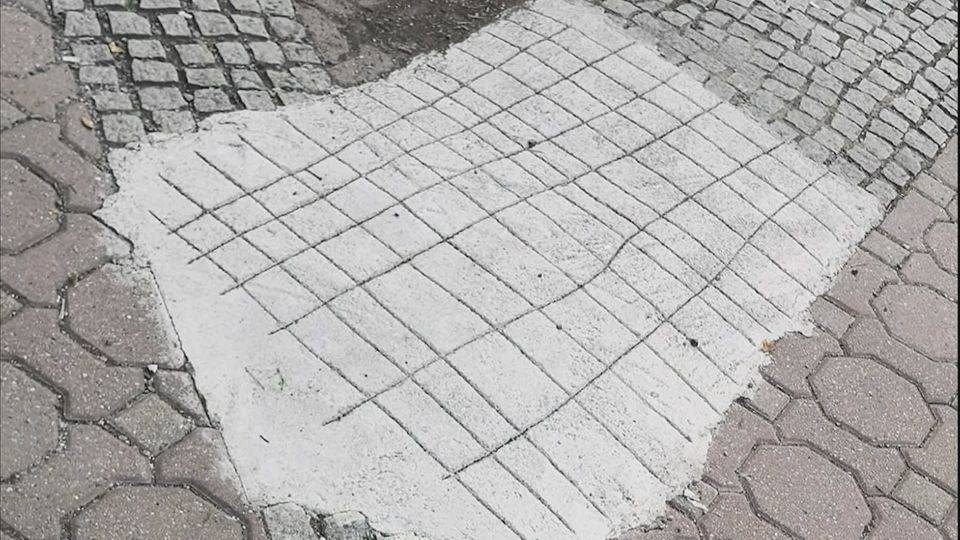 Nerovnomerný betónový záplat na chodníku so vzorovaným povrchom medzi kockami a hexagonálnymi dlaždicami.