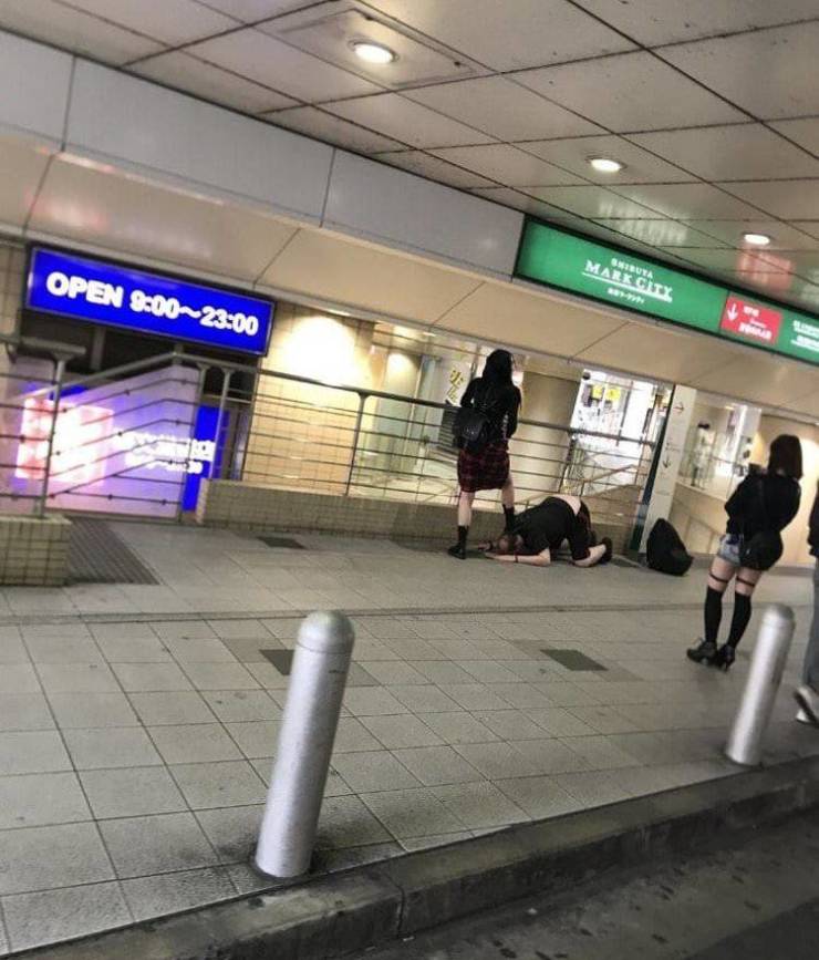 Skupina mladých ľudí v interiéri pri nápisoch s obchodnými hodinami, jedna osoba kľačí na zemi.