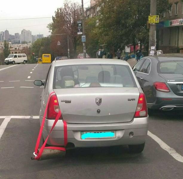 Auto s provizórnou opravou výfuku na mestskom parkovisku, zachytené počas dňa.