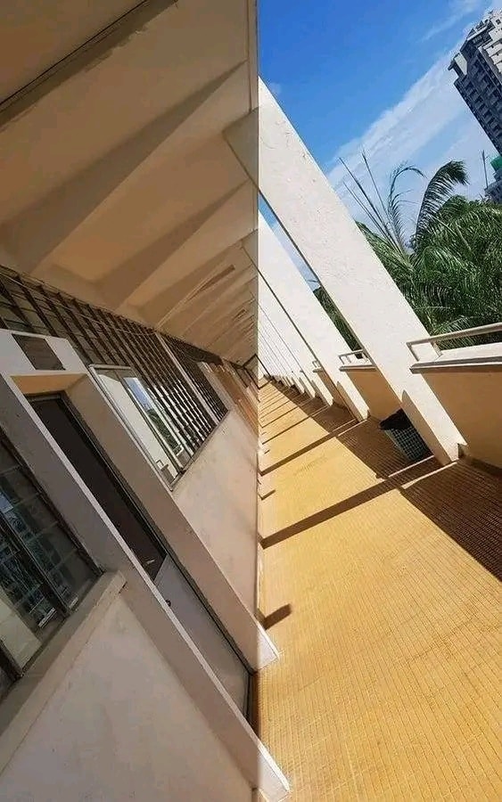 Pohľad na modernú architektúru s terasou, slnečný deň, obklopený vegetáciou a mestským pozadím.