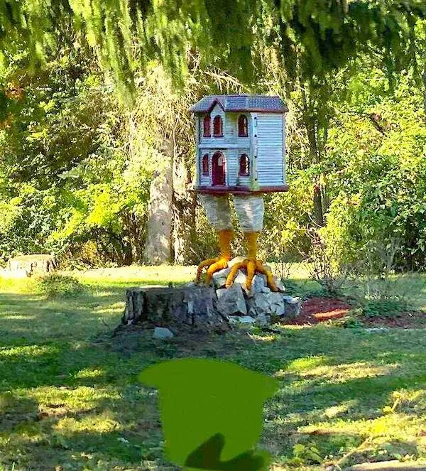 Dom na kuracích nohách v lese, inšpirovaný bájami, stojí na pníku obklopený zeleným prostredím.