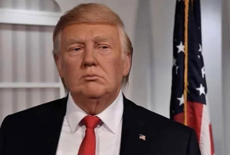 Osoba v saku a červenej kravate pri americkej vlajke v interiéri.