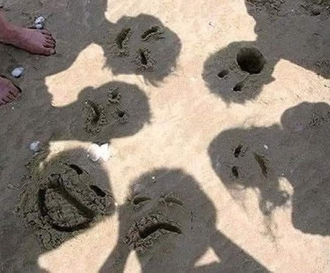 Tieňové tváre na piesku vytvarované ľudskými hlavami v kruhu na pláži.