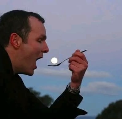 Muž s lyžičkou, ktorá nápadne vyzerá, akoby naberal Mesiac na oblohe, tvorí optickú ilúziu pri západe slnka.