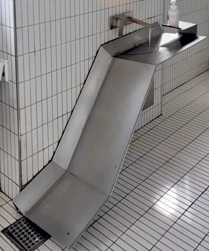 Nezvyčajný umývadlový sklz s vodovodom v dlaždicovej kúpeľni, vedľa fľaše s tekutým mydlom.