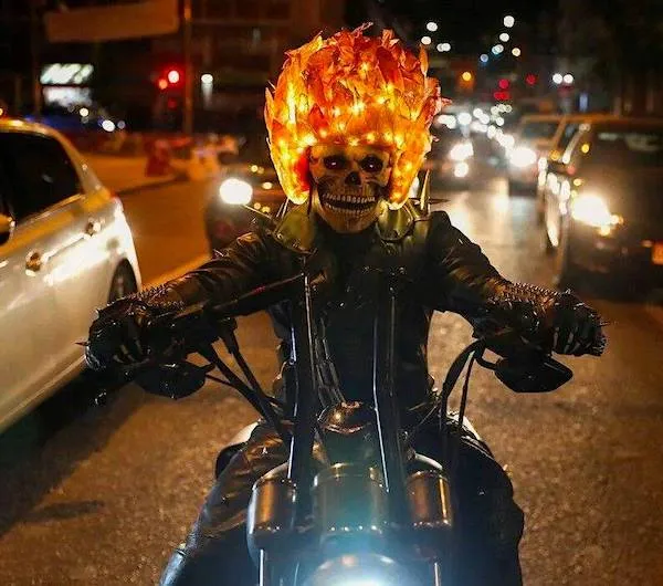 Motorkár s horiaciou lebkou na motorke v nočnej premávke, extravagantný outfit priláka pozornosť.