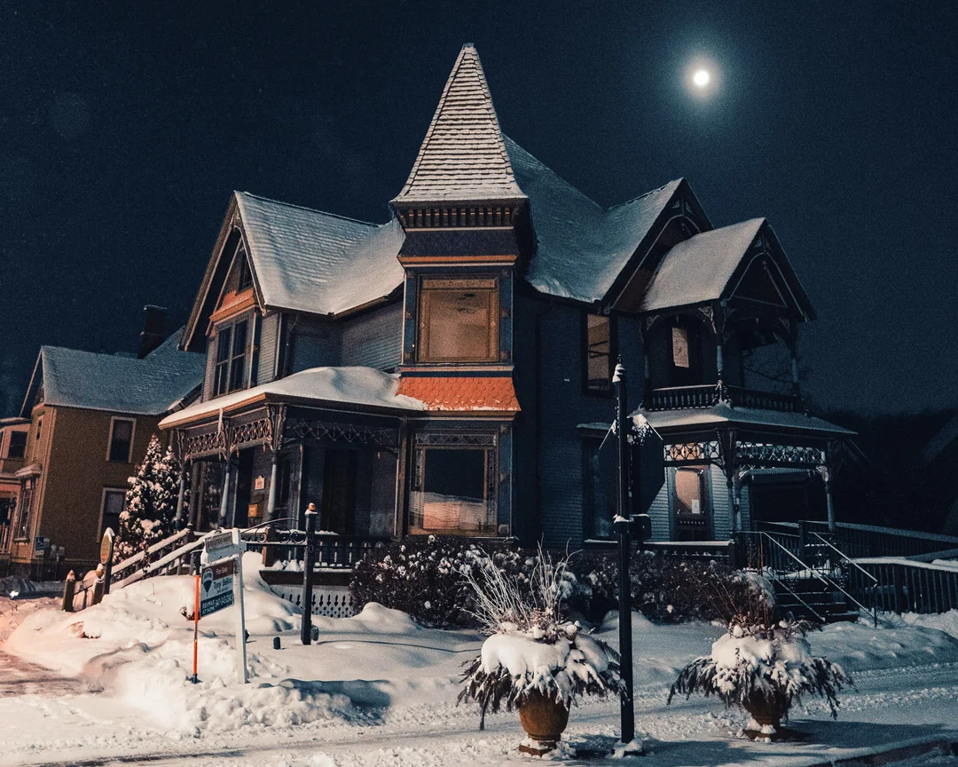 Nočný pohľad na historický dom so snehom na streche, osvetlený mesiacom.